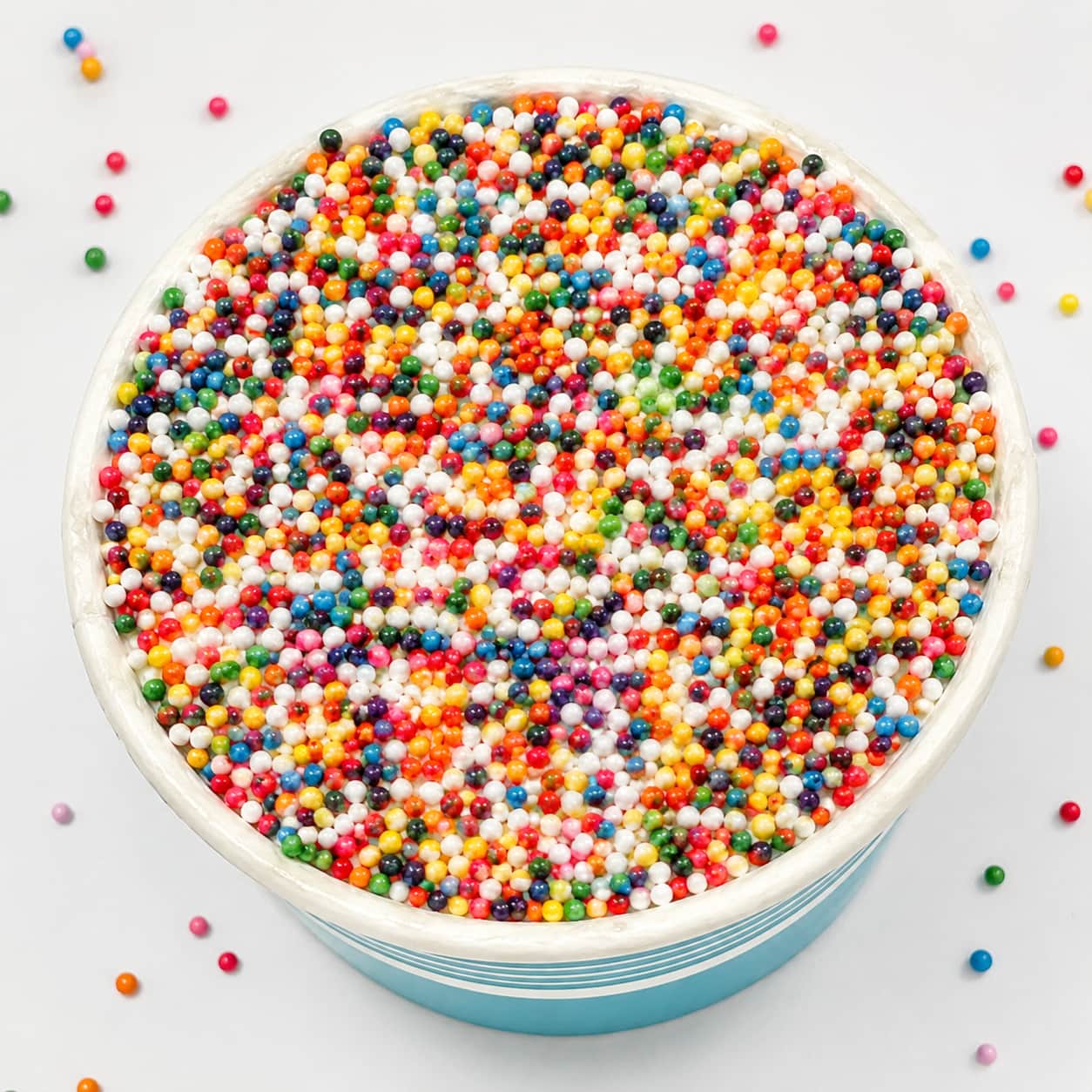 Overhead close-up of a Sprinkle Cake's rainbow nonpareil sprinkle top, with loose sprinkles scattered around
